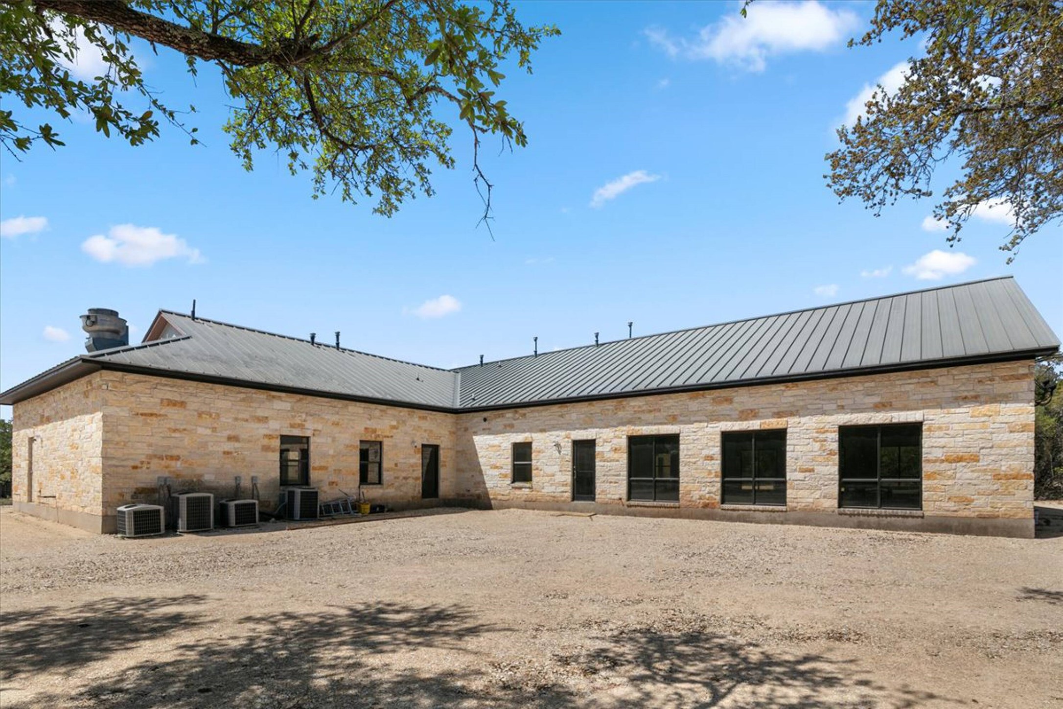 375 King Rea Spur Georgetown, TX 78633 - Photo 22 of 29 Exterior featuring a stone facade, a metal roof, dark-framed windows, and a gravel-covered area