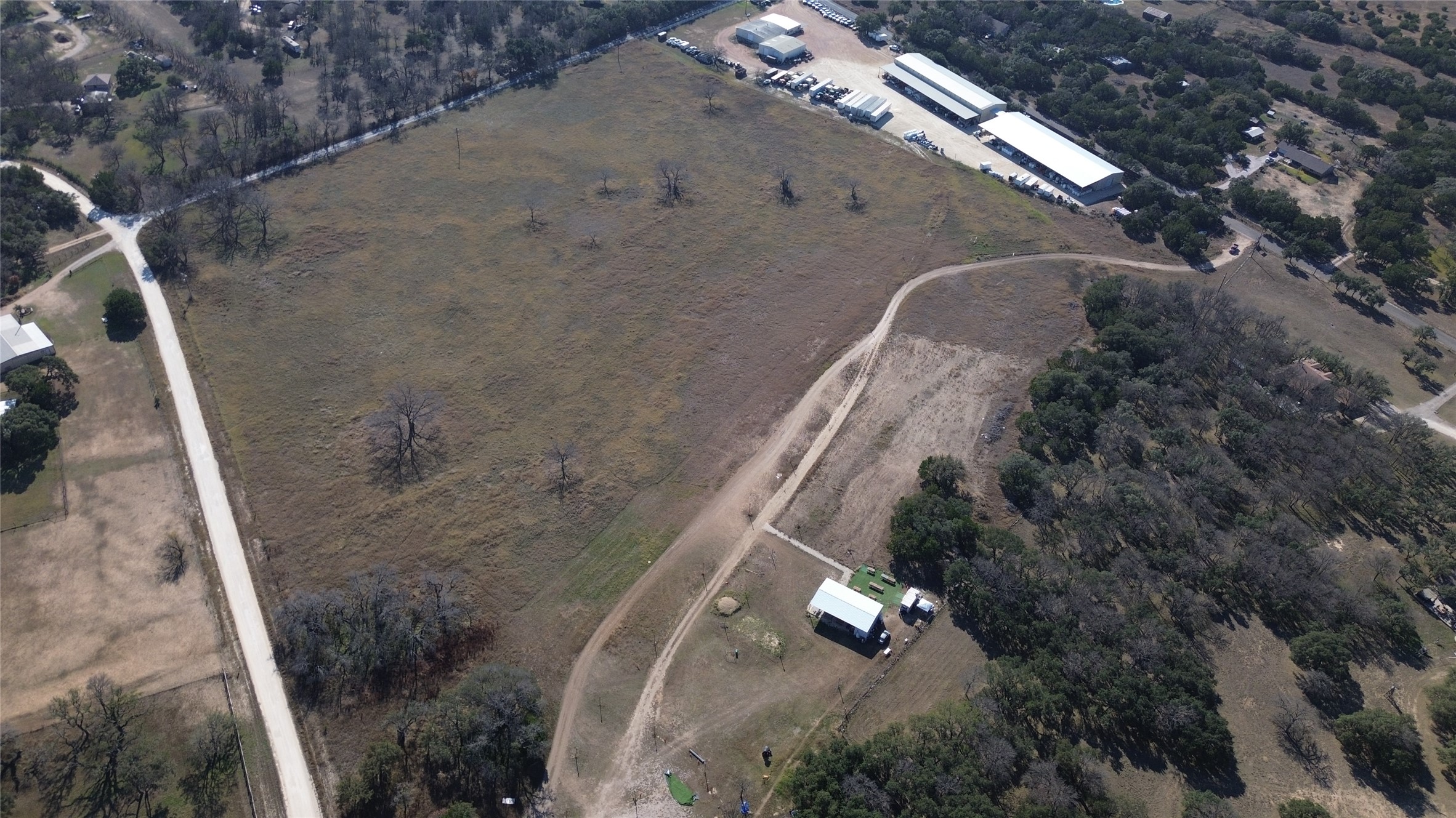 375 King Rea Spur Georgetown, TX 78633 - Photo 27 of 29 Expansive aerial view of a large land parcel featuring mixed terrain, a prominent unpaved road, and distant industrial buildings