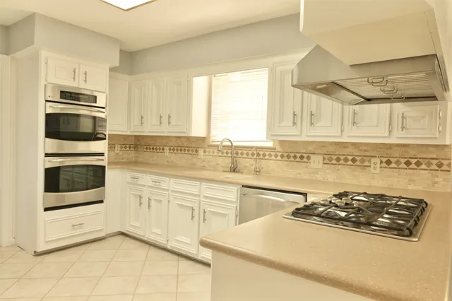 a kitchen with stainless steel appliances a stove a sink and white cabinets