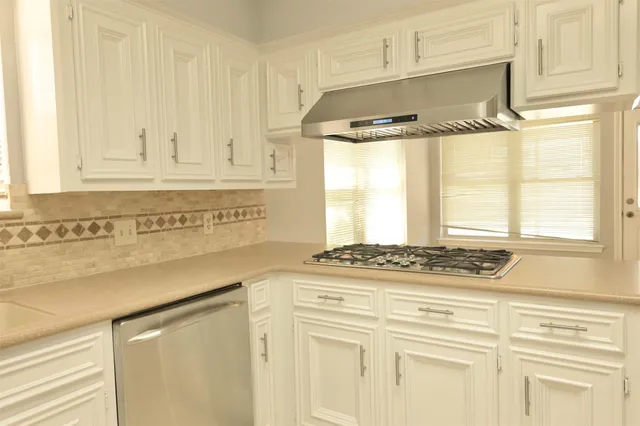 a kitchen with stainless steel appliances granite countertop white cabinets and a window