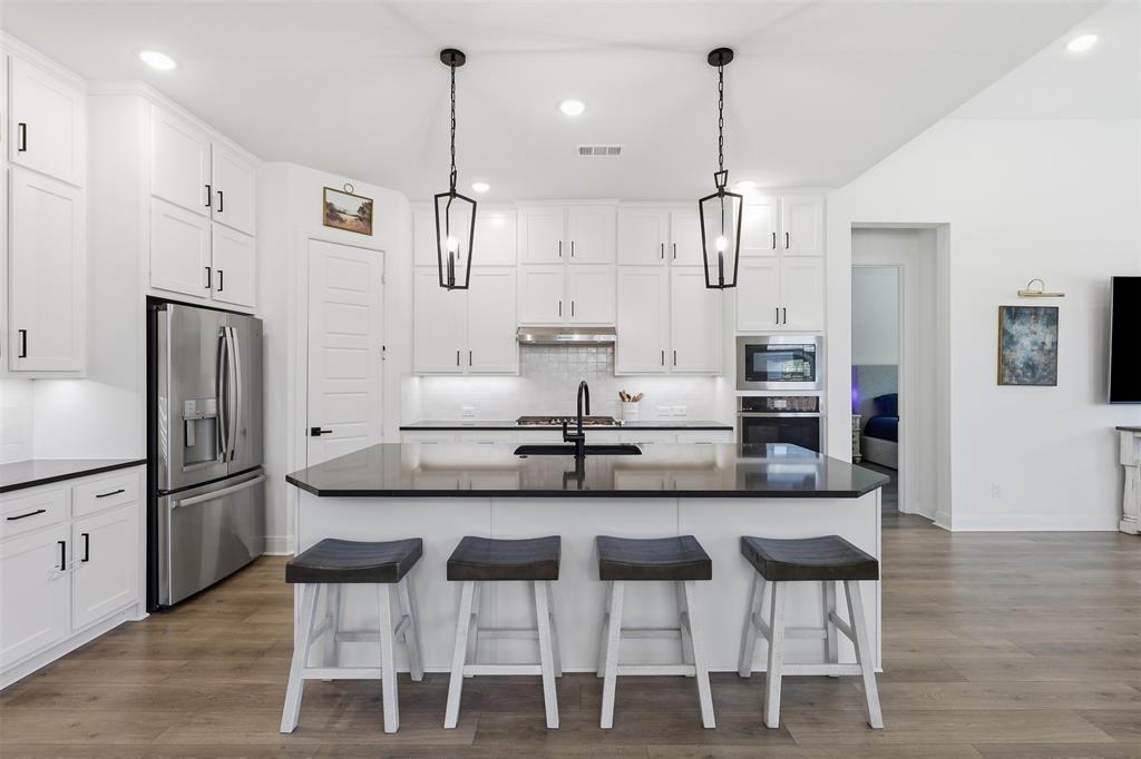 15413 Short Rdg Lane Fort Worth, TX 76008 - Photo 12 of 39 Open-concept kitchen featuring white cabinetry, a large central island with dark countertops, stainless steel appliances, and wood-finish flooring
