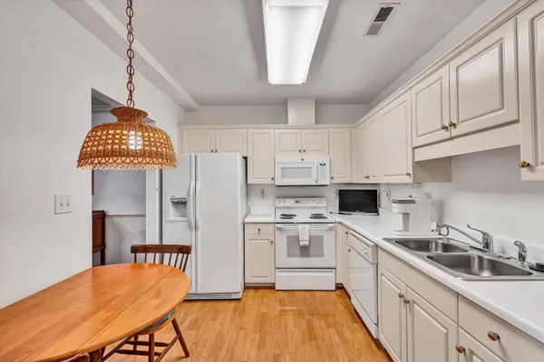 a kitchen with stainless steel appliances a stove a sink dishwasher a refrigerator with white cabinets and wooden floor