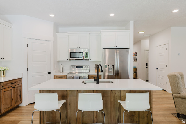 287 East 1000 North Logan, UT 84321 - Photo 11 of 41 Modern kitchen featuring a large central island with a sink, white countertops, stainless steel appliances, white upper cabinetry, and wood-finish lower cabinetry