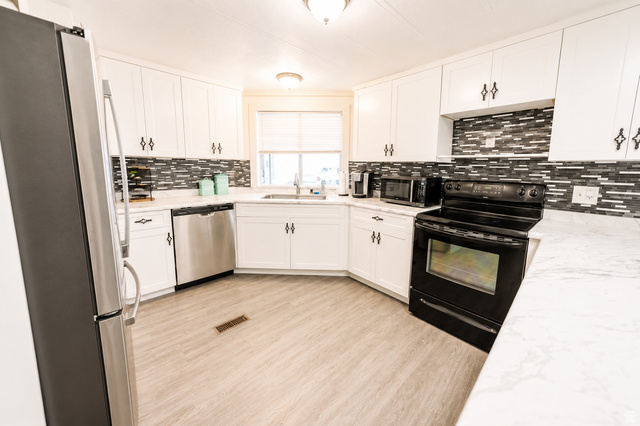305 West Elmo Road Elmo, UT 84521 - Photo 8 of 27 Kitchen featuring white cabinetry, gray and white mosaic tile backsplash, stainless steel dishwasher, black electric range, and wood-finish flooring