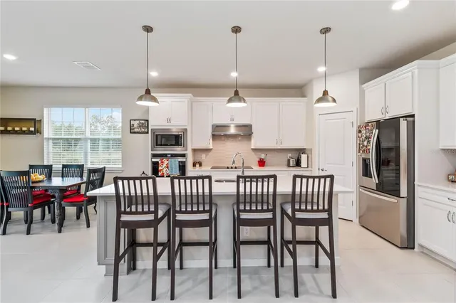 a kitchen with stainless steel appliances kitchen island granite countertop a dining table chairs and a view of living room