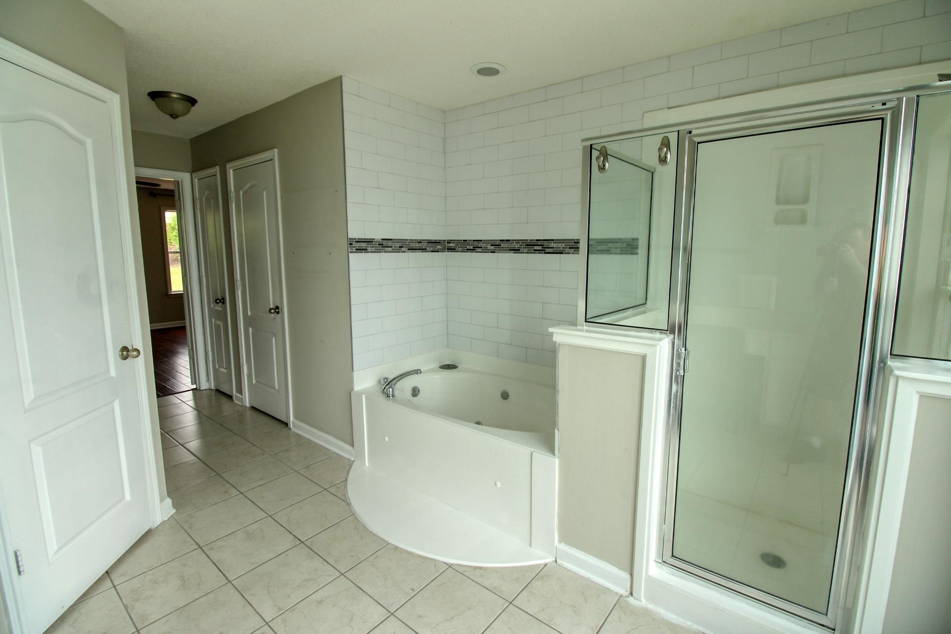 25 Whispering Ridge Cove Oakland, TN 38060 - Photo 14 of 20 Bathroom featuring a corner jetted tub, a separate glass-enclosed shower, white subway tile surround with decorative accent band, and square tile flooring