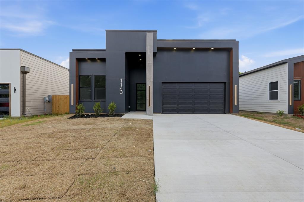 1143 Riverwood Road Dallas, TX 75217 - Photo 1 of 24 Contemporary gray exterior featuring a prominent garage, a streamlined entryway, and multiple windows