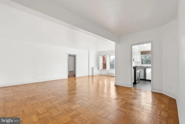 a view of empty room with wooden floor and kitchen