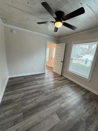 an empty room with wooden floor ceiling fan and windows