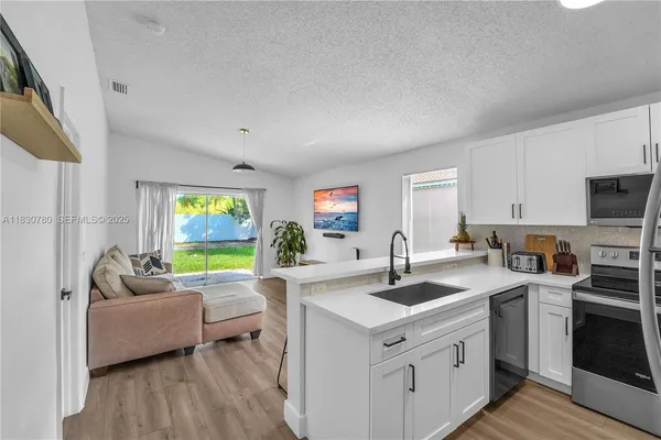 a living room with stainless steel appliances kitchen island granite countertop a sink a stove a dining table and chairs with wooden floor