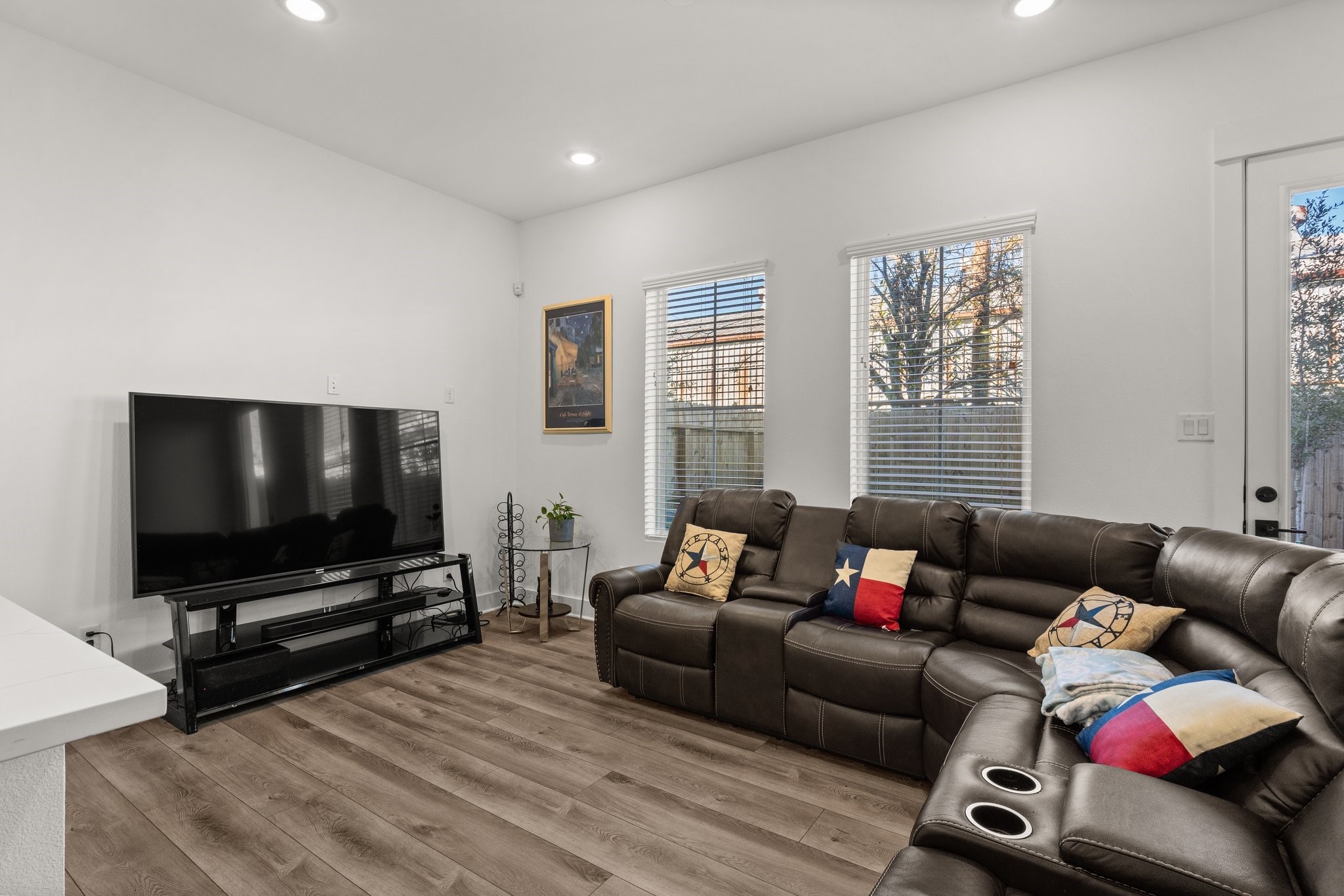 2928 Stevens Street Houston, TX 77026 - Photo 9 of 30 Cozy living room with sleek wood flooring and a large sectional sofa. Features a wall-mounted TV, natural light from two windows, and modern recessed lighting. Perfect for relaxation and entertainment.