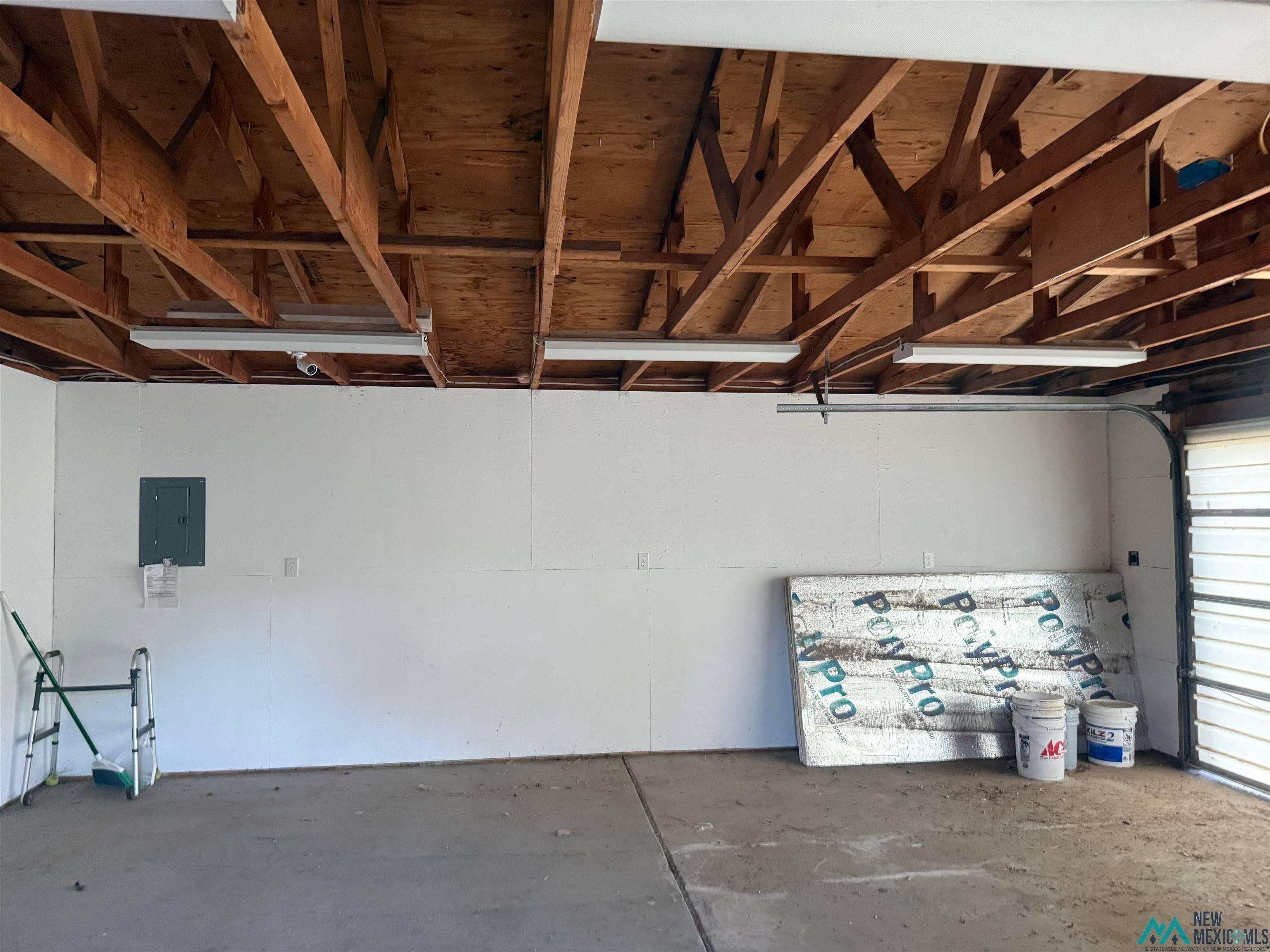 25 Linwood Road Raton, NM 87740 - Photo 3 of 41 Open garage space featuring exposed wood beam ceiling, concrete flooring, and fluorescent overhead lighting