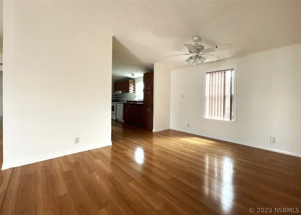 a view of an empty room and kitchen with wooden floor