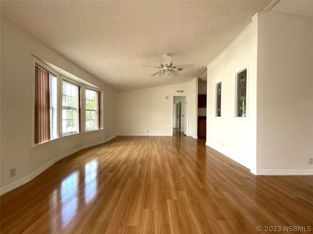 a view of an empty room with wooden floor and a kitchen