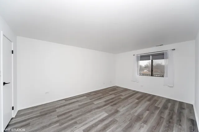 a view of an empty room with wooden floor and window