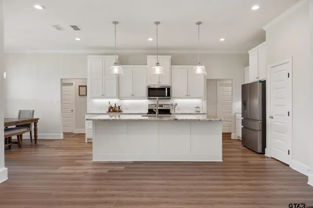 a large kitchen with stainless steel appliances kitchen island a refrigerator a stove a sink and a dining table with wooden floor