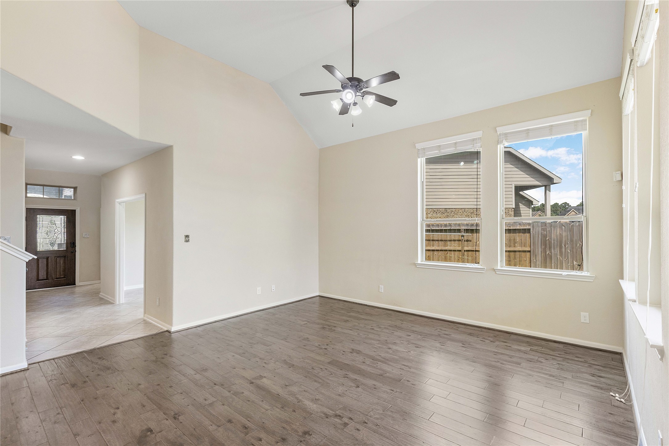 17206 Upper Ridge Lane Humble, TX 77346 - Photo 17 of 50 Bright living area with high ceilings, hardwood floors, and large windows. An open layout leads to a tiled entryway and front door. A ceiling fan adds comfort and style.