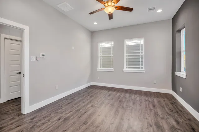 an empty room with wooden floor chandelier fan and windows