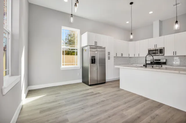 a kitchen with stainless steel appliances granite countertop a refrigerator a sink dishwasher a stove and white countertops with wooden floor