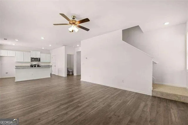 a view of an empty room with wooden floor and a ceiling fan