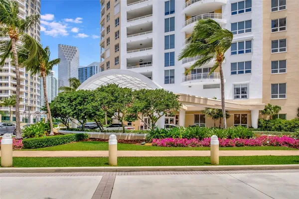 a front view of a multi story residential apartment building with yard and bench and plants