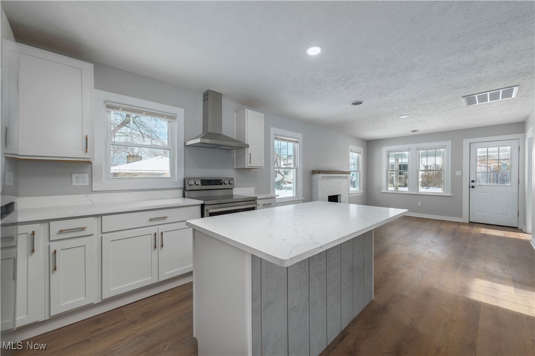 218 Roxboro Road Vermilion, OH 44089 - Photo 15 of 50 Kitchen featuring a center island, stainless steel range with electric stovetop, wall chimney range hood, white cabinets, and light stone counters