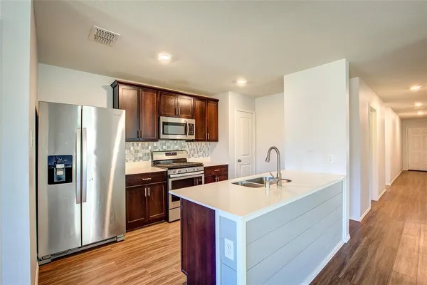 a kitchen with a sink stainless steel appliances and wooden floor