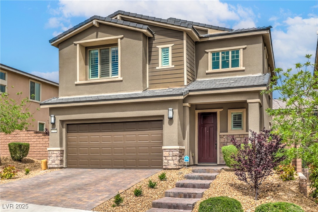 View of front of property featuring stone siding, an attached garage, stucco siding, and decorative driveway