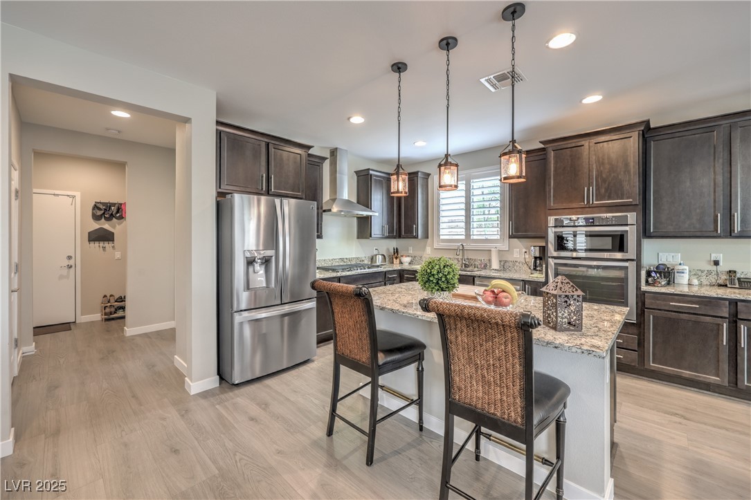 2711 Evolutionary Lane Las Vegas, NV 89138 - Photo 11 of 37 Kitchen with appliances with stainless steel finishes, wall chimney range hood, dark brown cabinets, light wood-style flooring, and recessed lighting