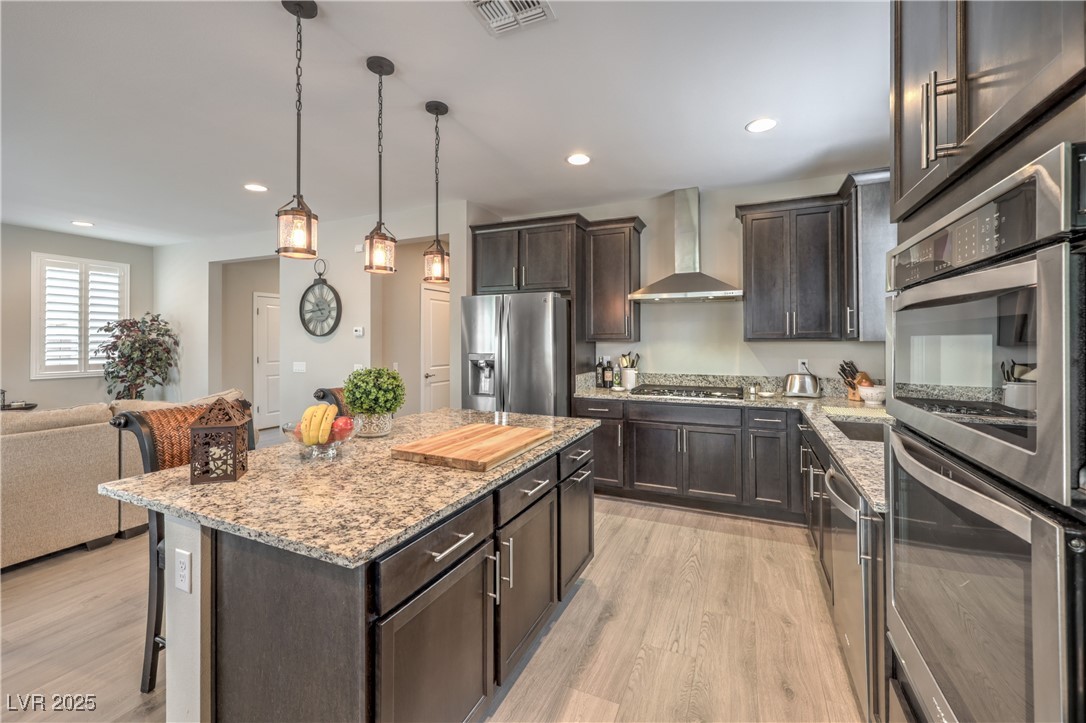 2711 Evolutionary Lane Las Vegas, NV 89138 - Photo 12 of 37 Kitchen with stainless steel appliances, wall chimney range hood, a kitchen bar, light wood-style floors, and dark brown cabinetry