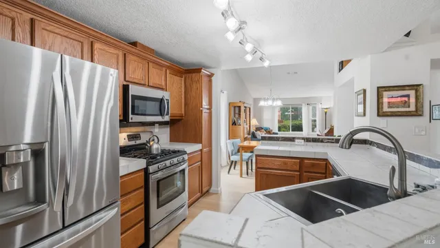 a kitchen with stainless steel appliances granite countertop a refrigerator a stove a sink dishwasher a dining table and chairs with wooden floor