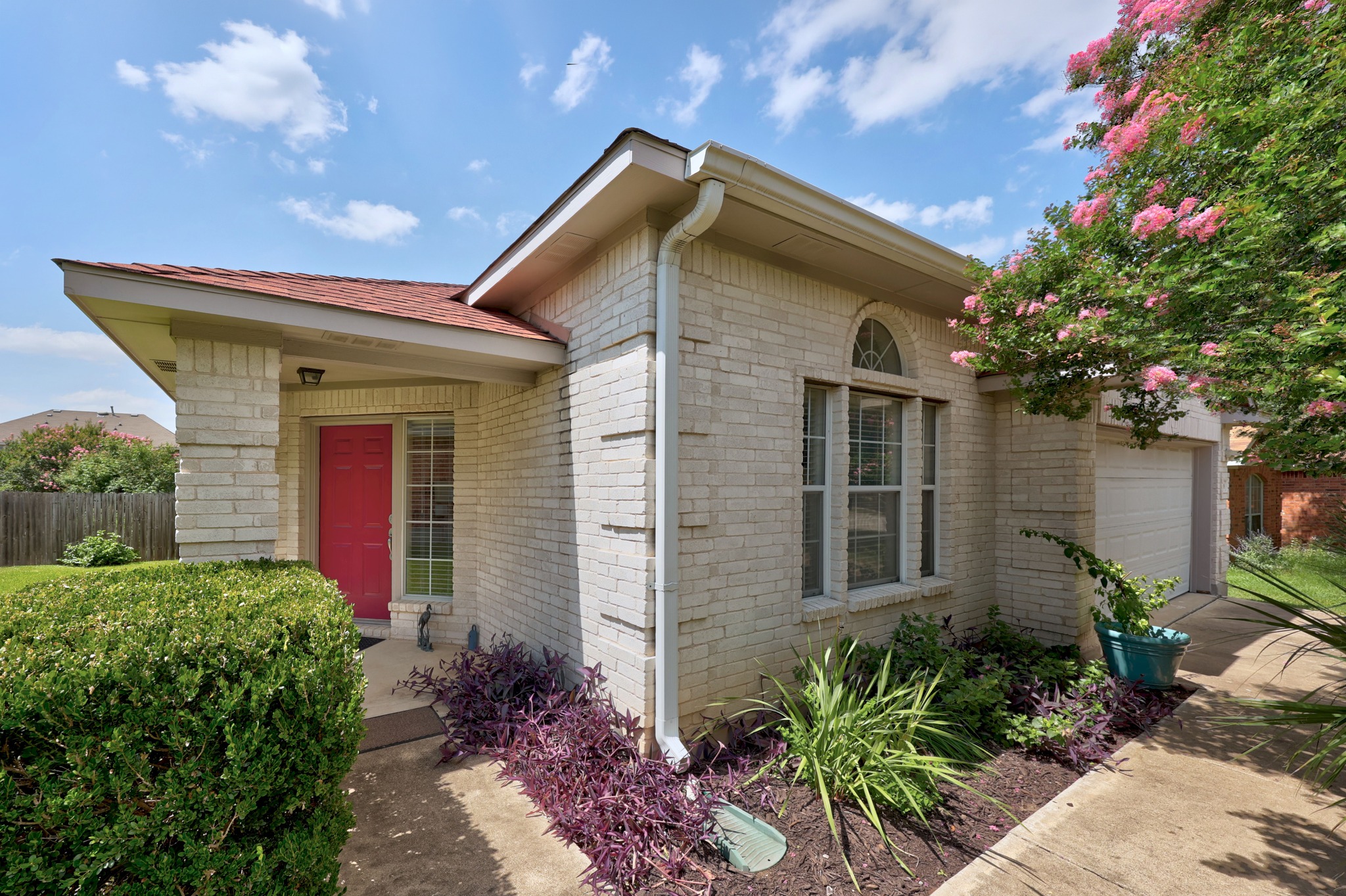 A cream brick facade welcomes with a vibrant front door and well-maintained landscape.