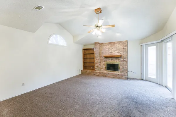 an empty room with windows fireplace and fan