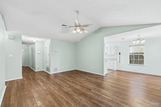 a view of an empty room with chandelier fan and wooden floor
