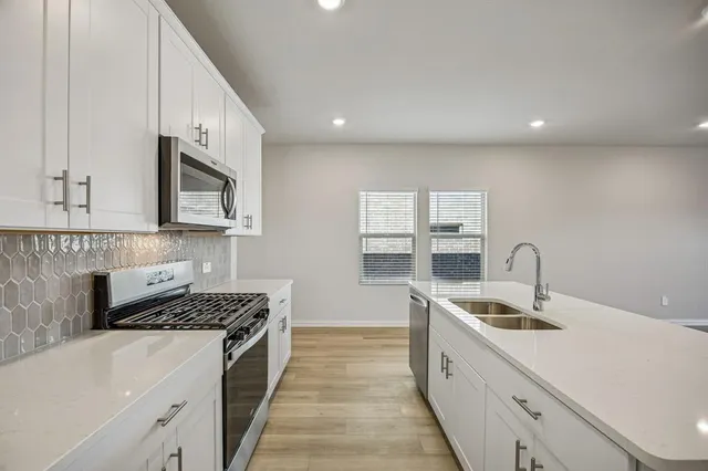 a kitchen with stainless steel appliances granite countertop a sink stove and white cabinets with wooden floor