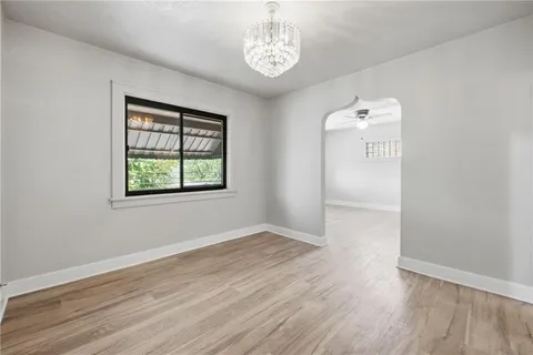 an empty room with wooden floor chandelier and windows