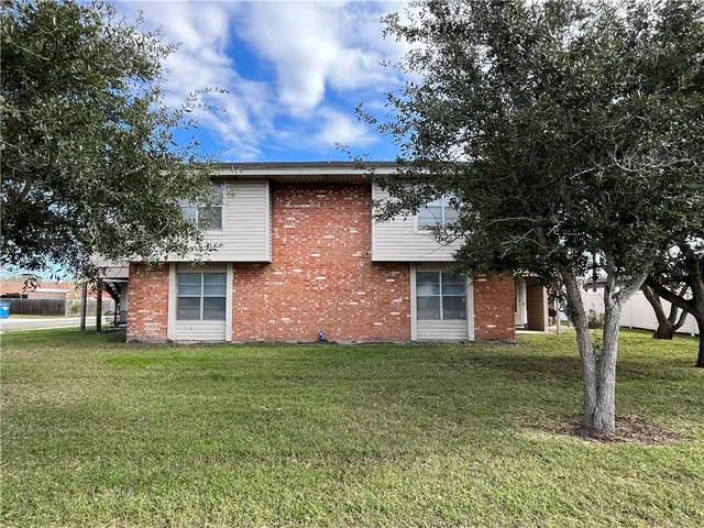 a brick house with a yard and large trees