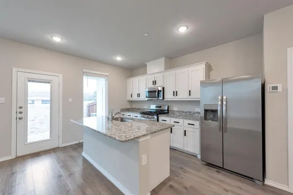 a kitchen with stainless steel appliances granite countertop a refrigerator a sink dishwasher a stove and white countertops with wooden floor