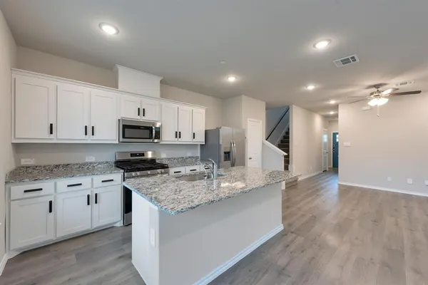 a kitchen with stainless steel appliances granite countertop a sink a stove a refrigerator and white cabinets with wooden floor