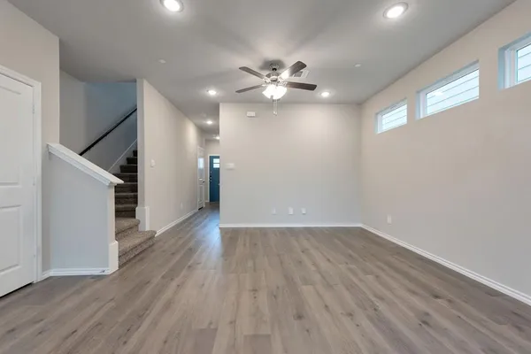 a view of an empty room with wooden floor and a ceiling fan