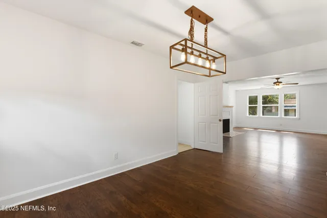 an empty room with wooden floor chandelier and windows