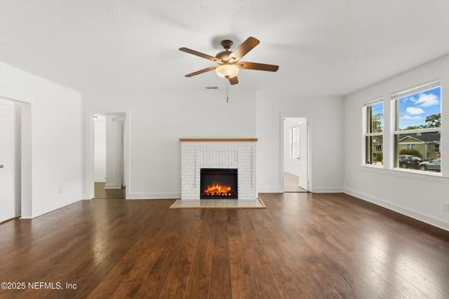 a view of an empty room with wooden floor fireplace and a window