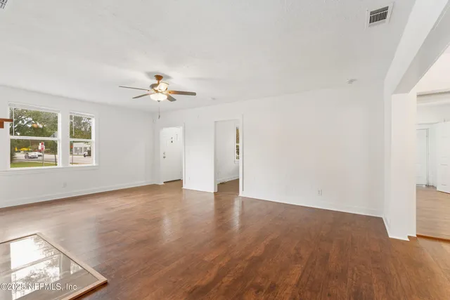 an empty room with wooden floor chandelier fan and windows