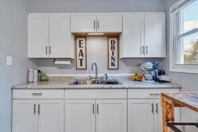 a kitchen with stainless steel appliances granite countertop a sink white cabinets and a window