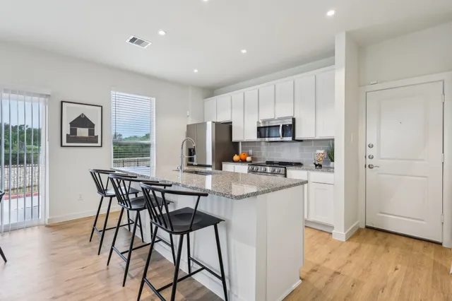 a kitchen with stainless steel appliances granite countertop a stove a sink a microwave a refrigerator and white cabinets with wooden floor