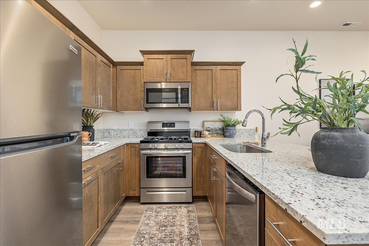 1445 North Bluffs Ridge Lane Boise, ID 83704 - Photo 25 of 47 Kitchen with appliances with stainless steel finishes, light stone countertops, brown cabinets, light wood-style flooring, and a peninsula