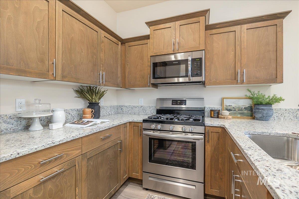 1445 North Bluffs Ridge Lane Boise, ID 83704 - Photo 5 of 47 Kitchen with appliances with stainless steel finishes, brown cabinetry, and light stone counters