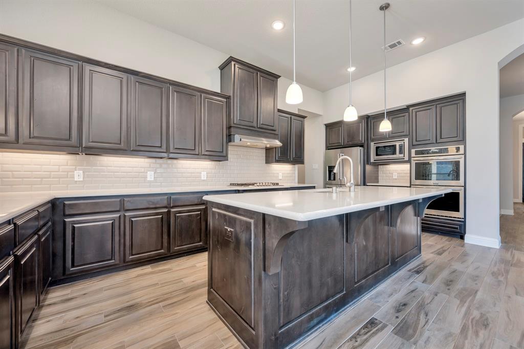 9820 Surveyor Road Little Elm, TX 75068 - Photo 9 of 40 Kitchen with arched walkways, decorative light fixtures, stainless steel appliances, light wood finished floors, and an island with sink