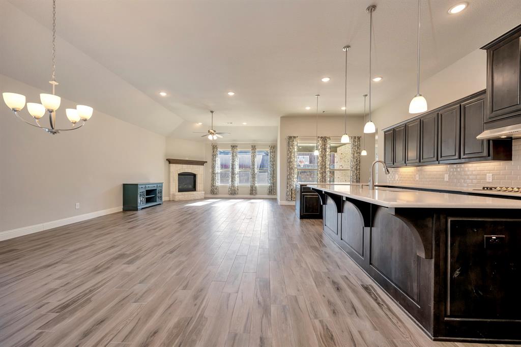 9820 Surveyor Road Little Elm, TX 75068 - Photo 39 of 40 Kitchen featuring hanging light fixtures, ceiling fan, a glass covered fireplace, open floor plan, and a kitchen island with sink