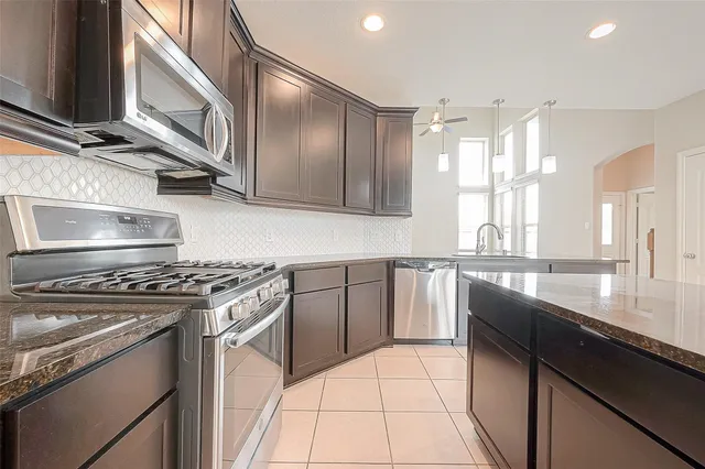 a kitchen with stainless steel appliances granite countertop a sink a stove and a wooden cabinets